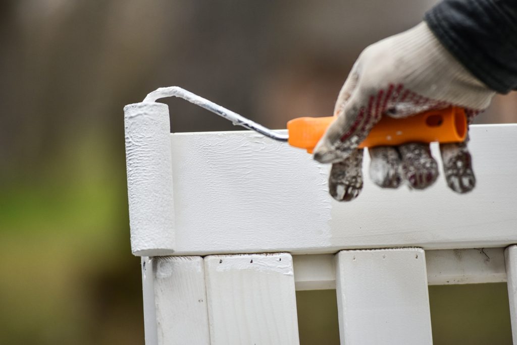 Man paints garden furniture white with a paint roller