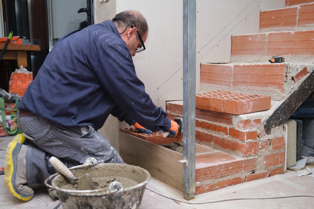 Bricklayer building a brick staircase in a home interior.