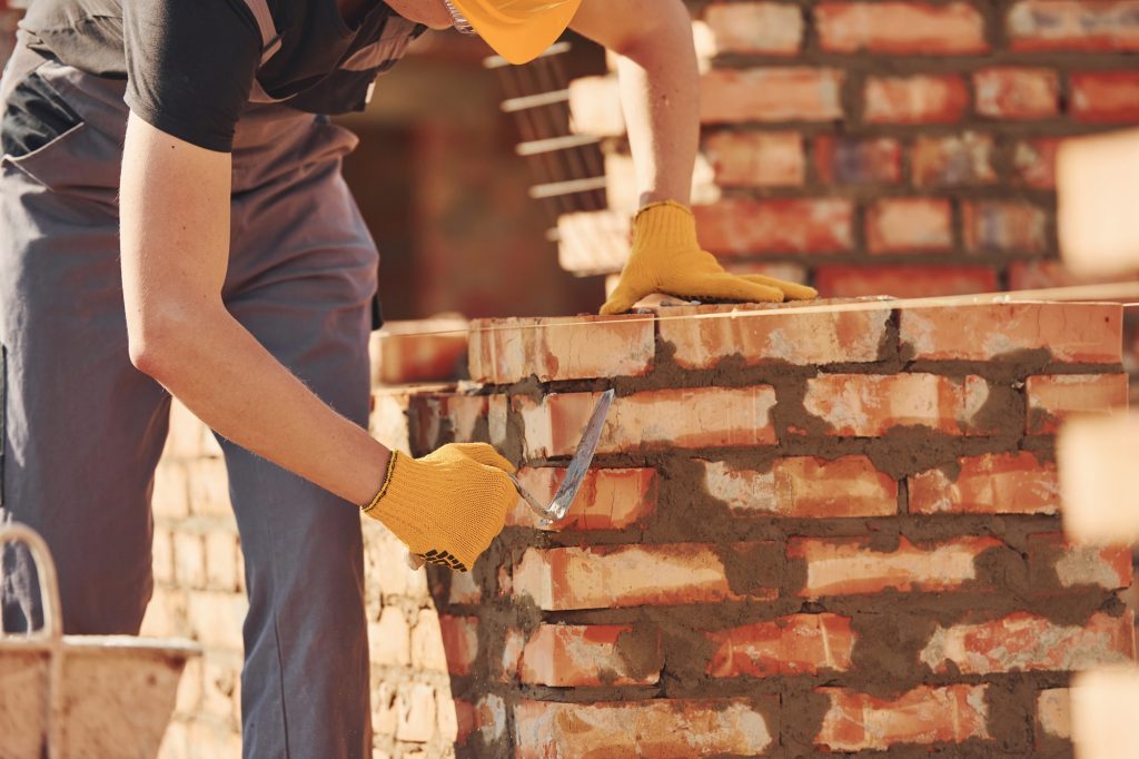 Busy with brick wall. Construction worker in uniform and safety equipment have job on building