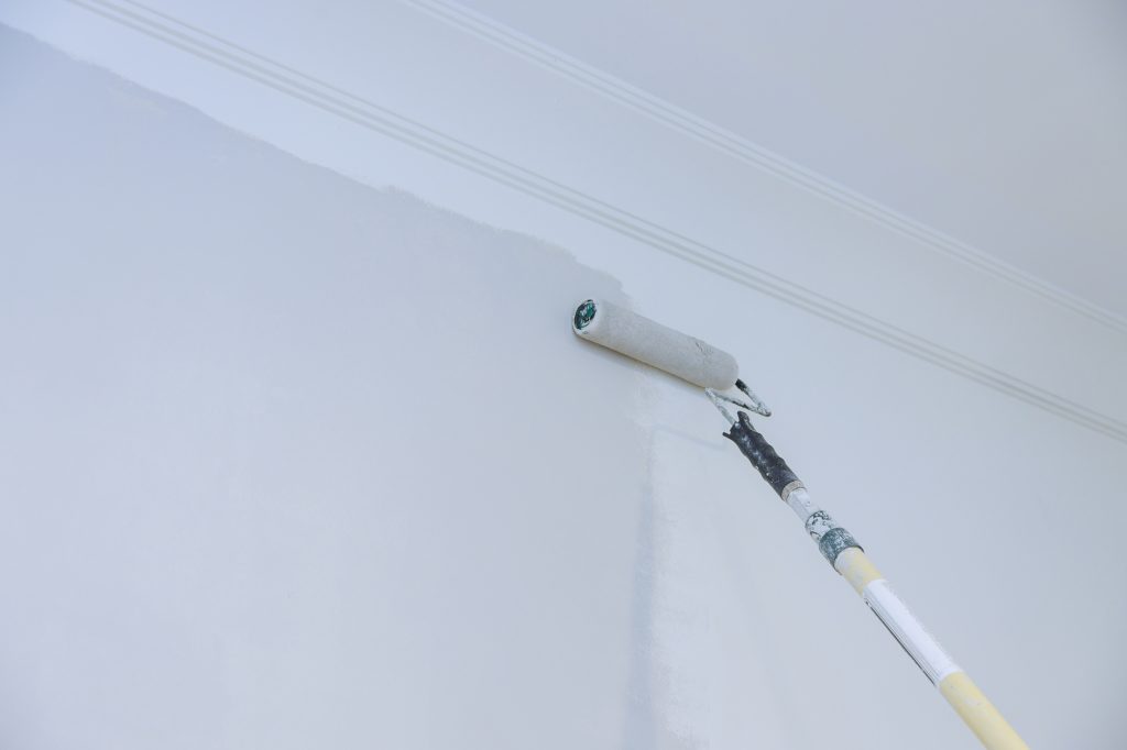 View of painter man painting the wall, with paint roller on empty space